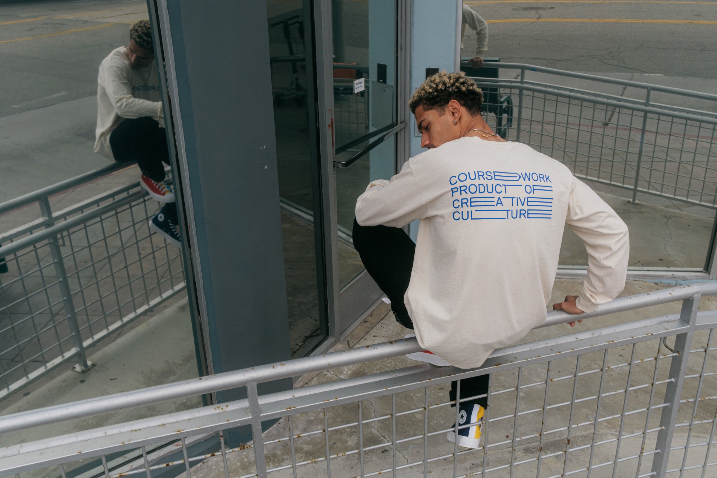 Model wearing the Full Width Text Long Sleeve Tee and sitting on a handrail.