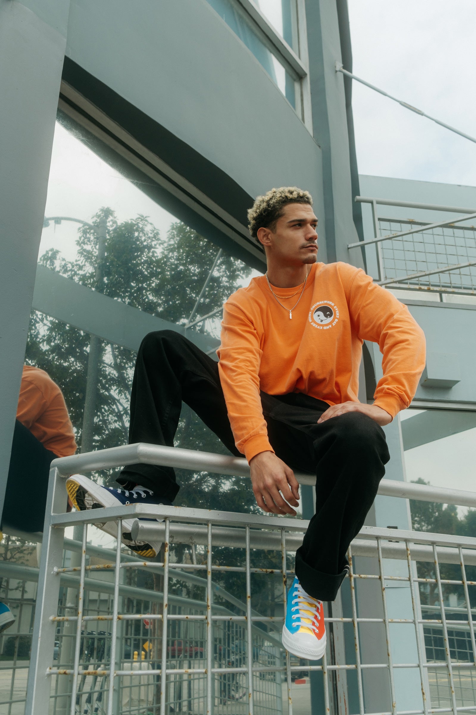 Model wearing the Day and Night Long Sleeve Tee in orange and sitting on a handrail.