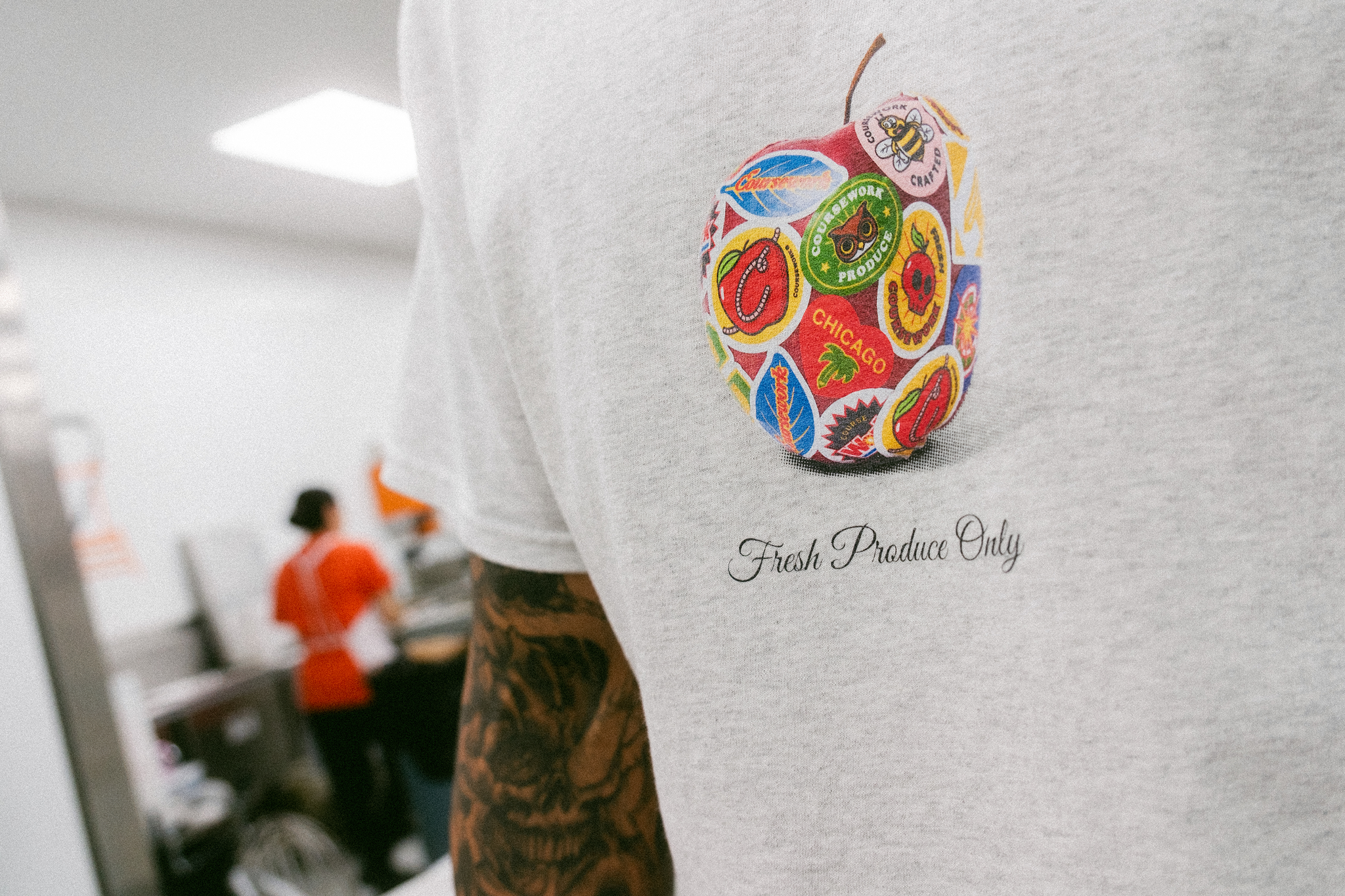 Close up shot of the Super Fresh Tee graphic of an apple with fruit stickers plastered all over it.