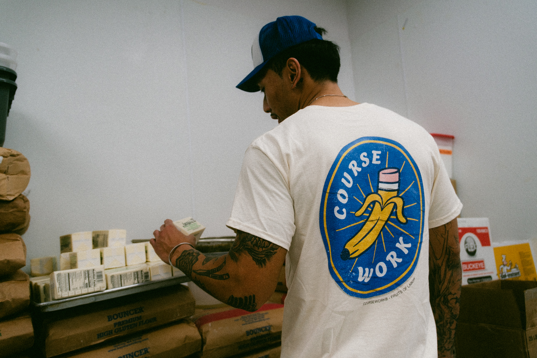 Model stands with back facing camera and is looking at sticks of butter in the kitchen of a bakery