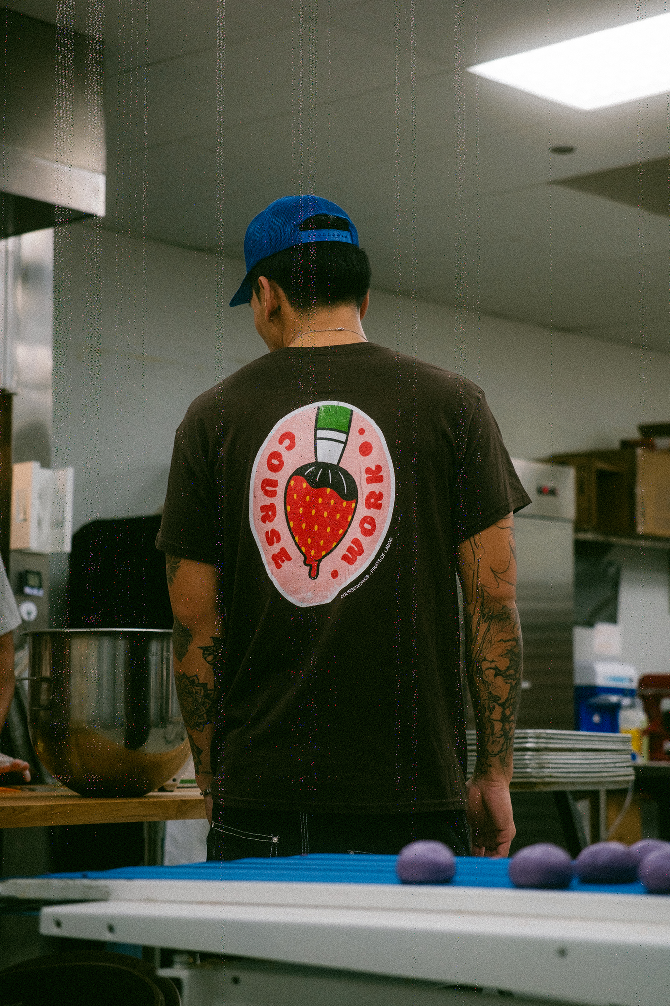 Model stands in kitchen of bakery with back facing camera and showing a fruit sticker graphic