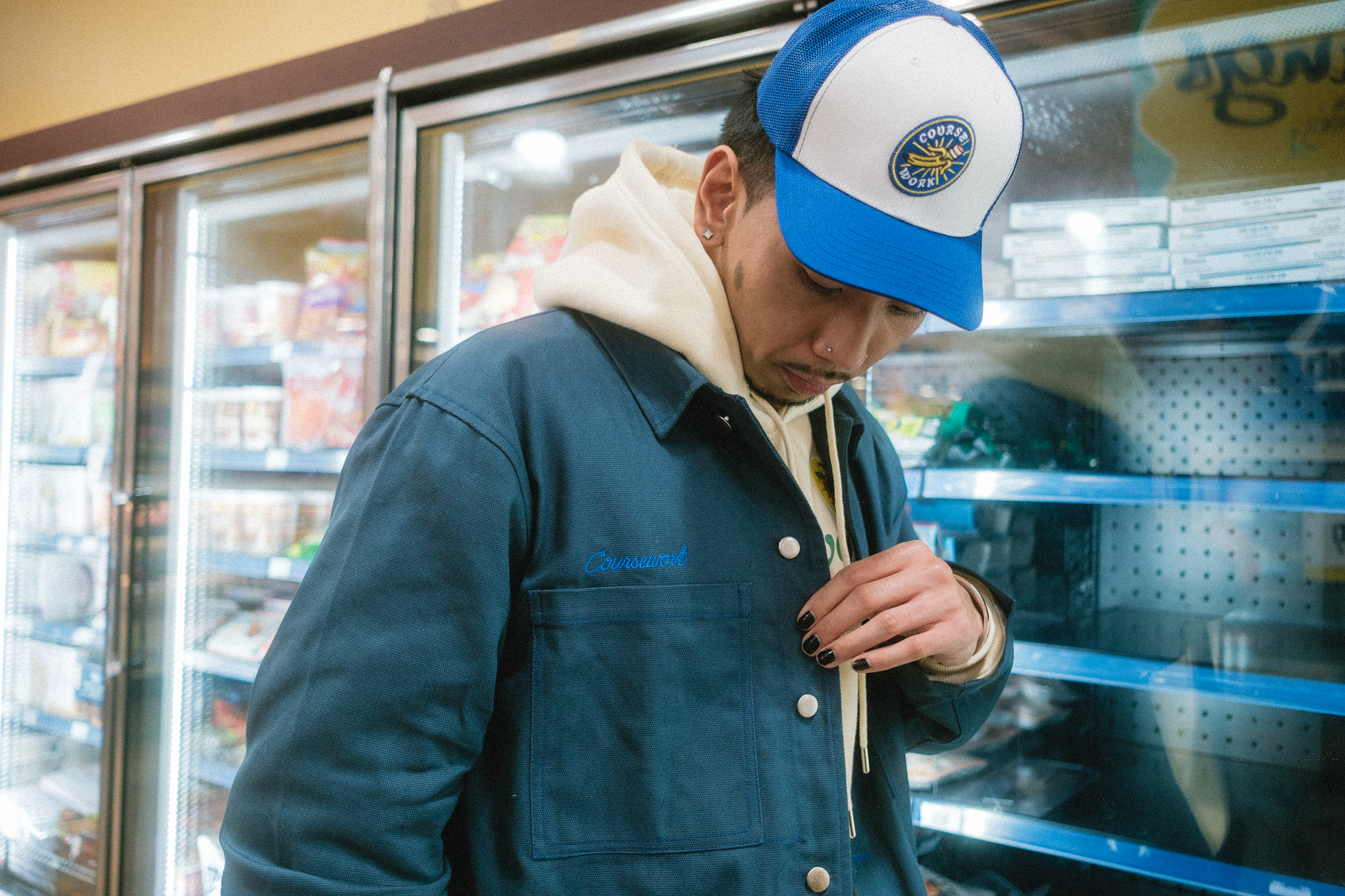 Model standing by refrigerated doors of grocery store and looking at the details of the Work Jacket