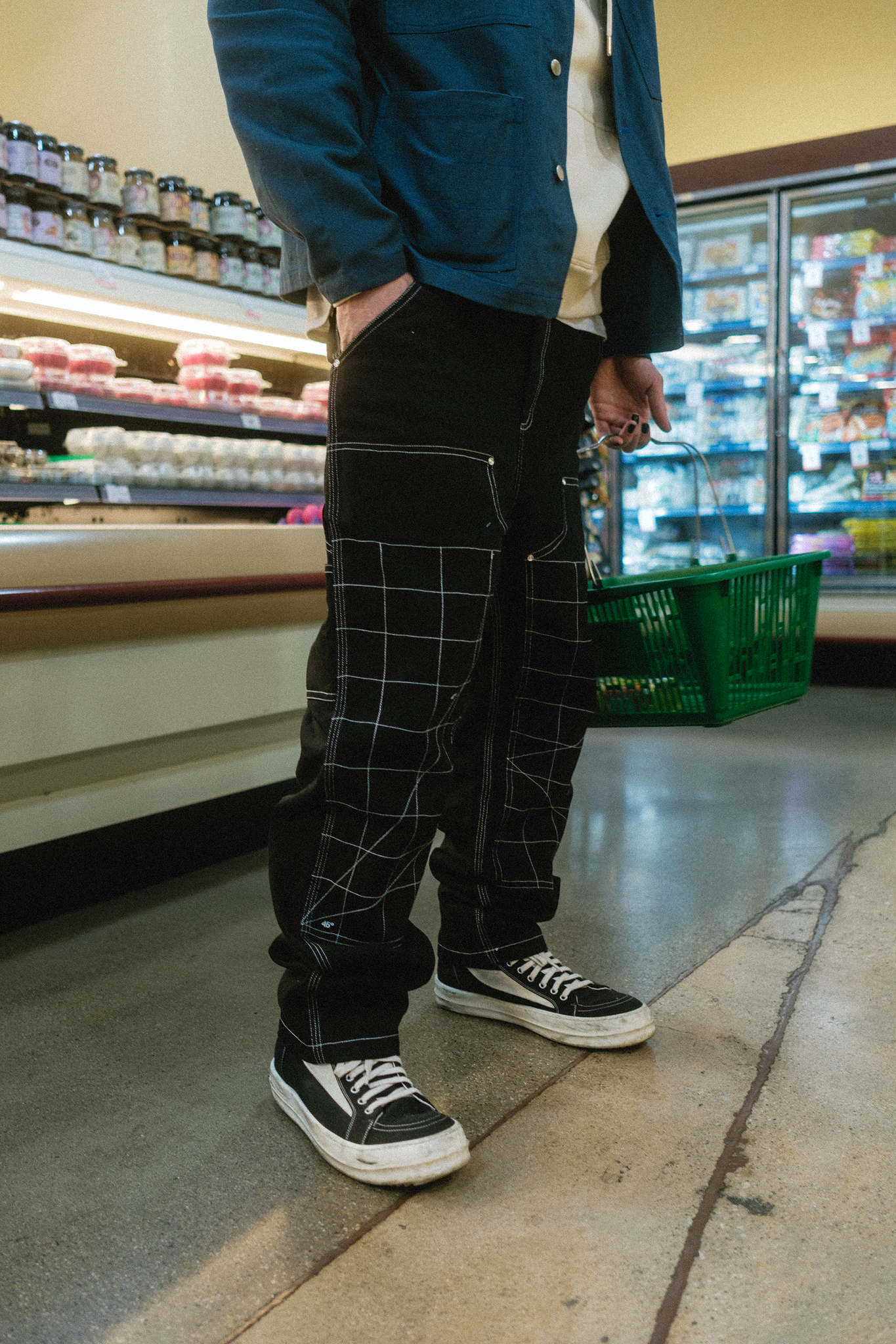 Shot of the Double Knee Work Pant in the meat section of the grocery store with model holding a basket in hand.