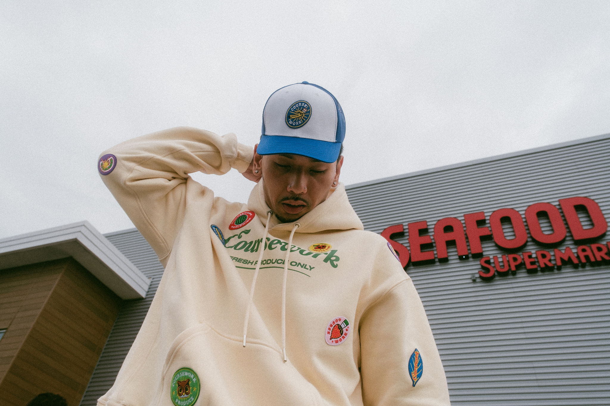 Upward shot of model adjusting hood of sweatshirt with the view of the sky and building behind him